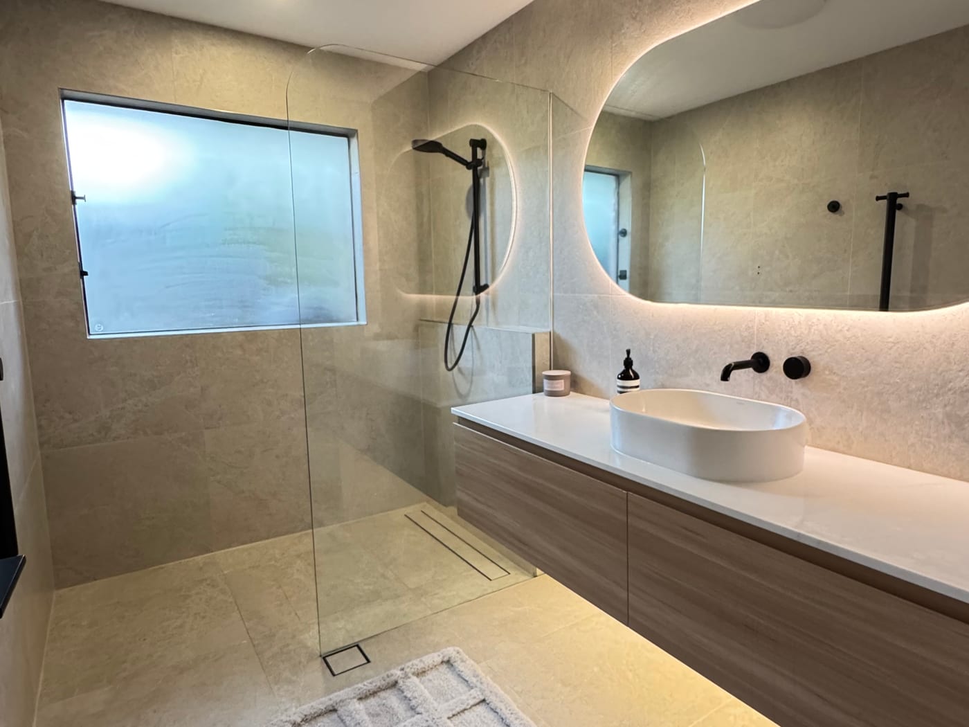 Renovated bathroom with a floating vanity, backlit mirror and walk-in shower