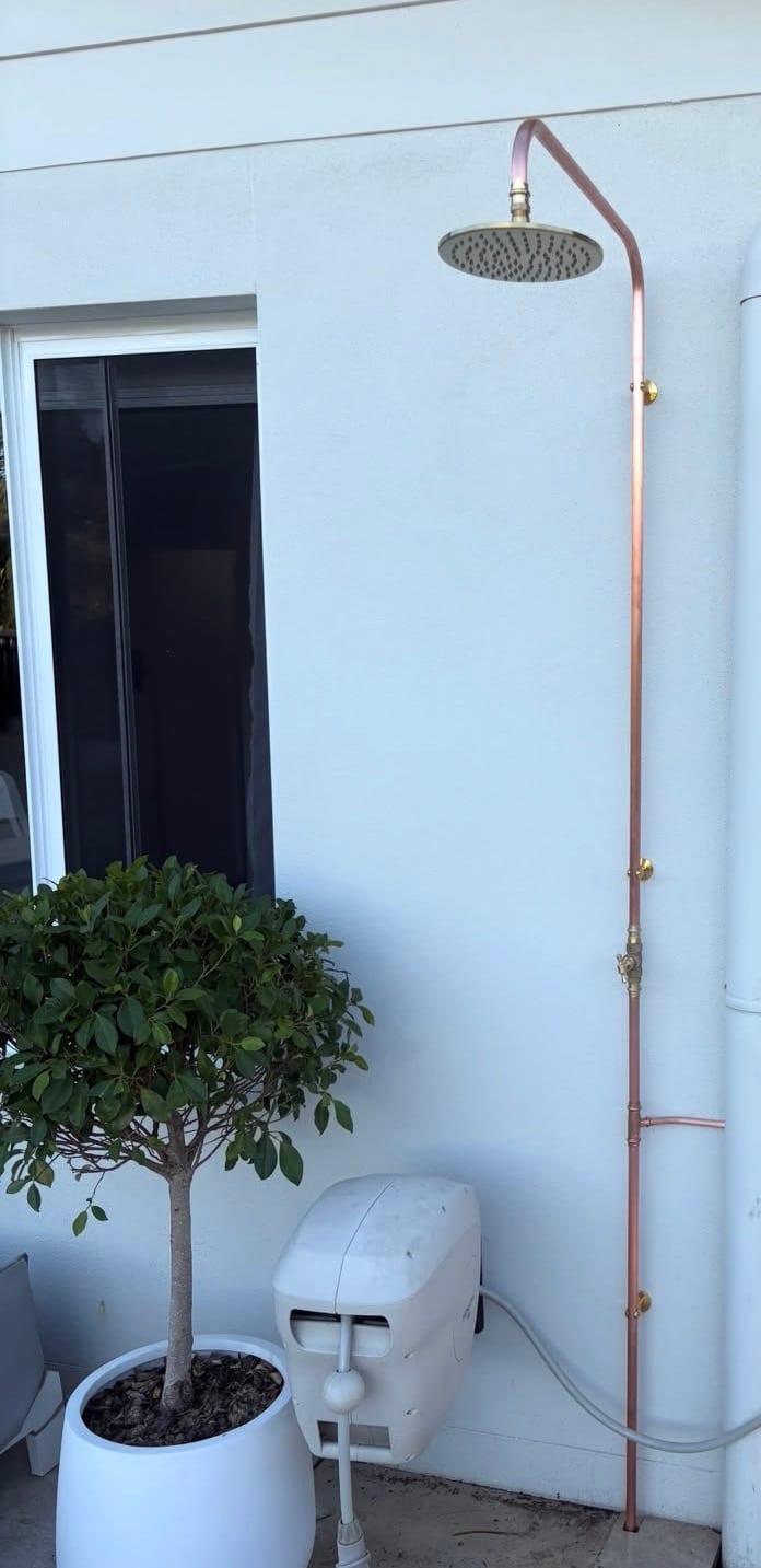 Outdoor copper shower plumbed against a white rendered wall